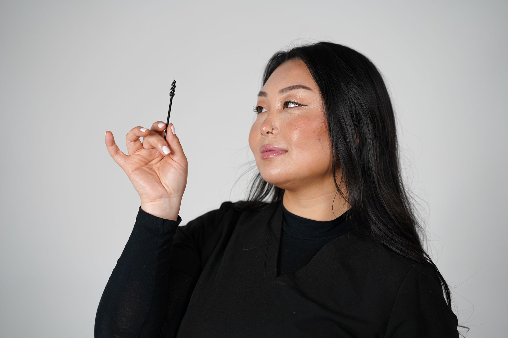 Woman in a black top holding up a small makeup brush against a plain light background