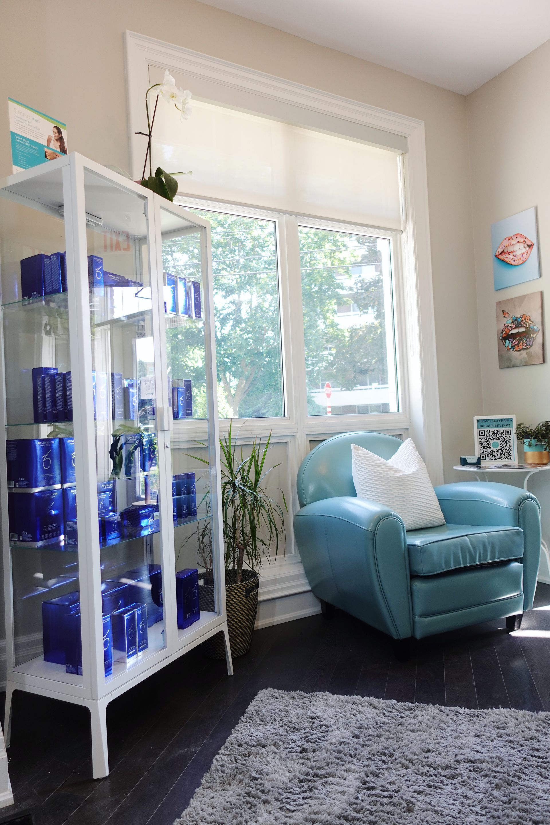 A bright room with a display shelf of blue objects, a blue chair by a window, and a rug.