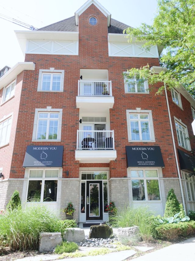 Red brick apartment building with balconies, awnings, and stone accents; surrounded by greenery.