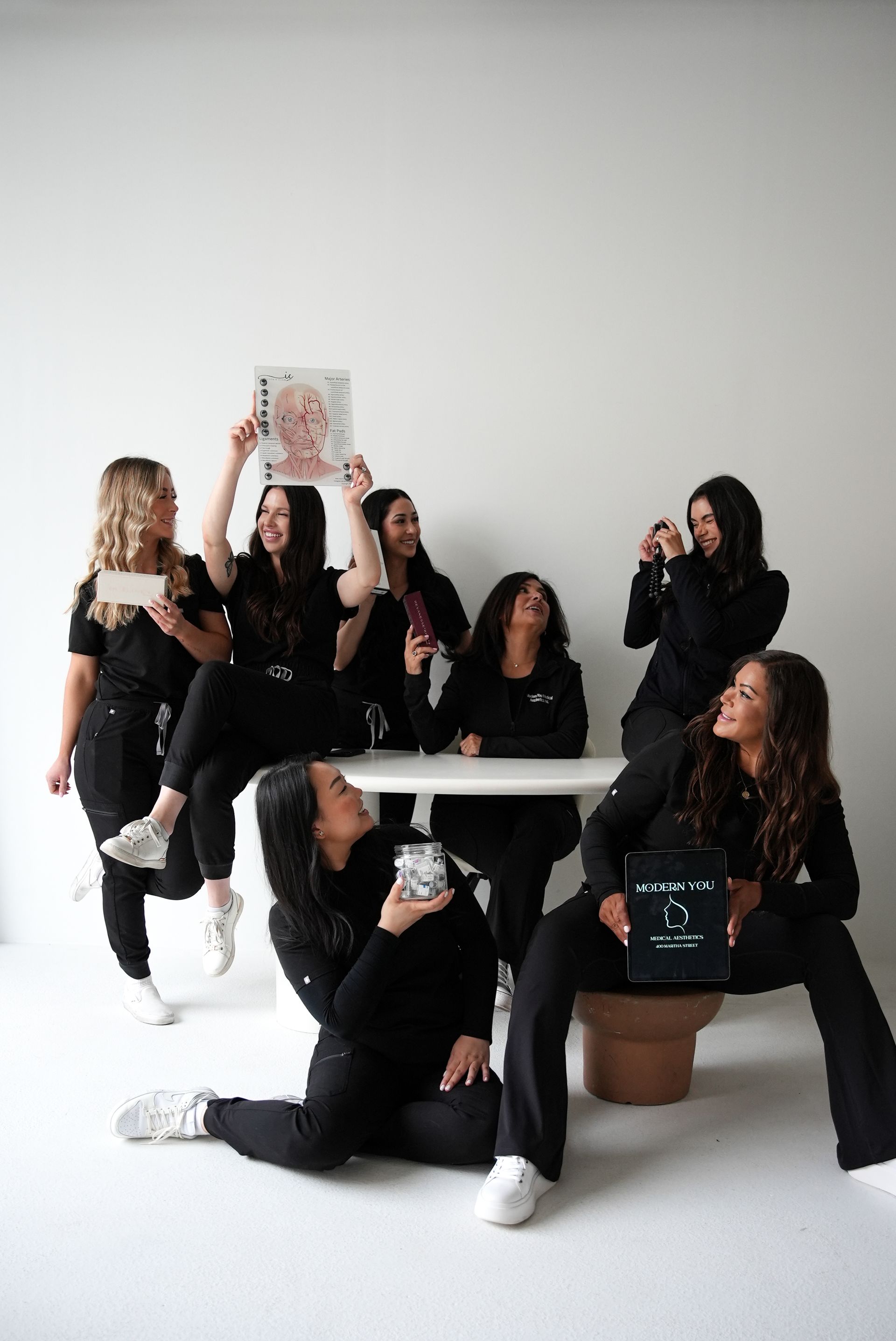 Group of women in black scrubs pose around a white table in a white room.