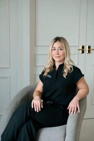 Blonde woman with wavy hair smiles. Indoors, neutral background.