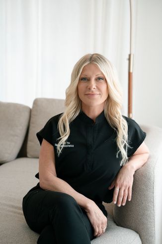 Blonde woman with blue eyes, smiling slightly, wearing a black shirt in front of a light-colored background.