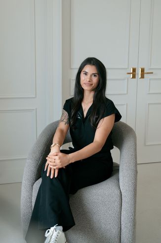Woman with long dark hair, smiling, holding a camera on a tripod, indoors against a white background.