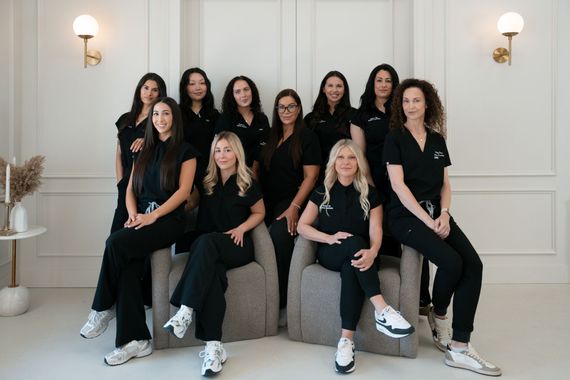 Eight women in white tops and jeans, holding hands, smiling, in a studio.