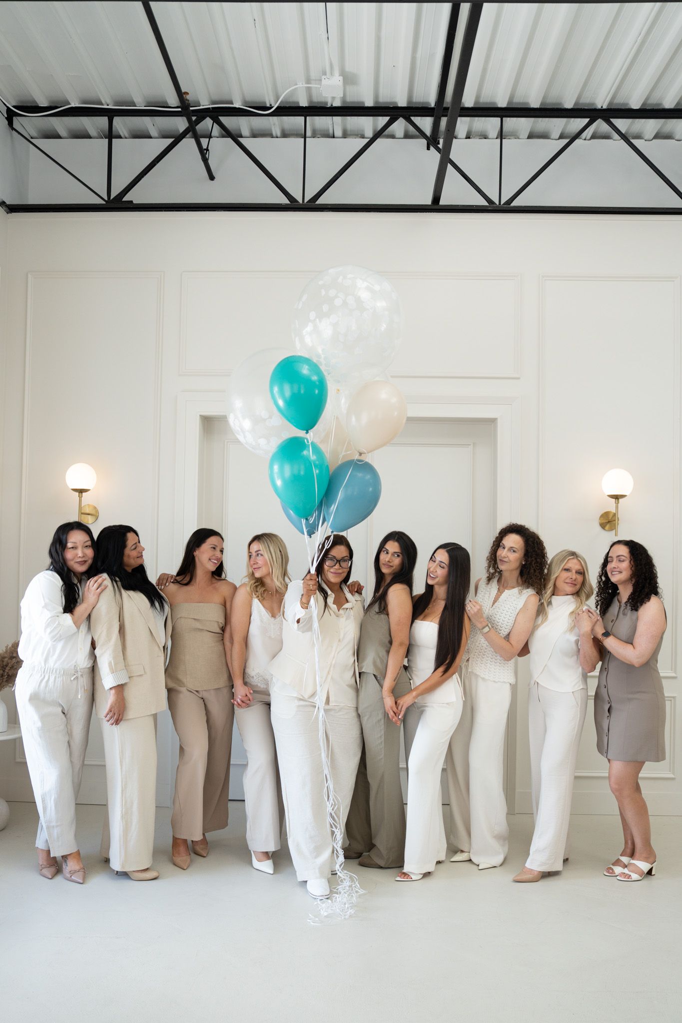 Eight women holding hands, wearing white tops and blue jeans, smiling, in a studio setting.