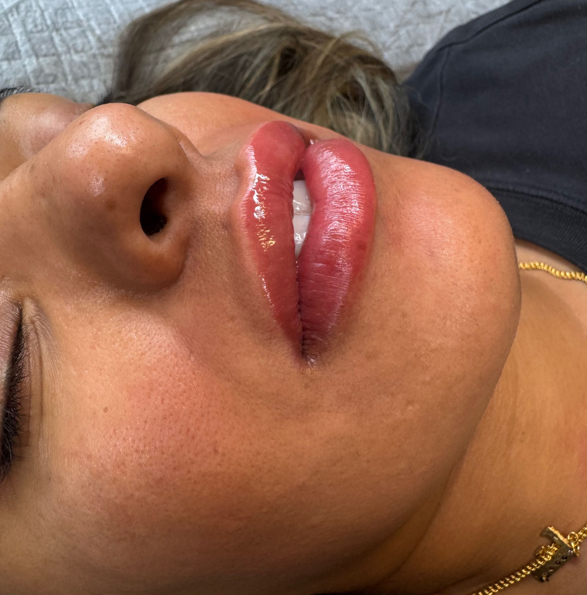 Close-up of a person’s face with glossy pink lips and visible nose piercing