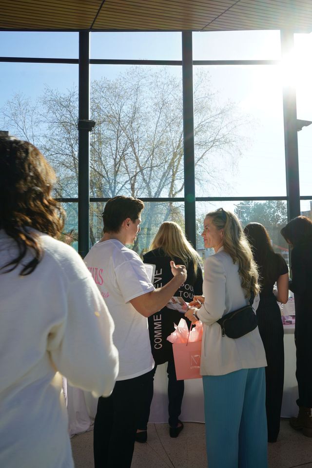 People chatting in a sunlit room with large windows and trees outside