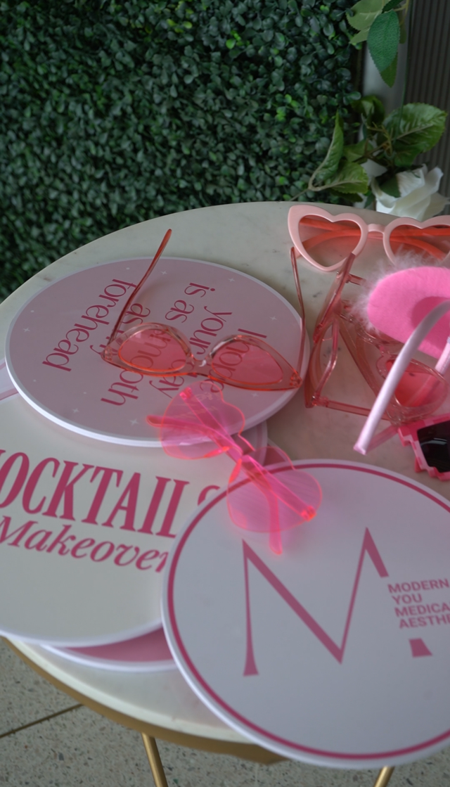 Pink cocktail-themed tableware on a round white table with greenery in the background