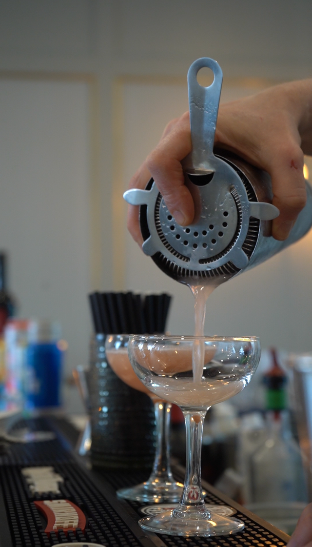 Bartender pouring a clear drink through a strainer into a martini glass
