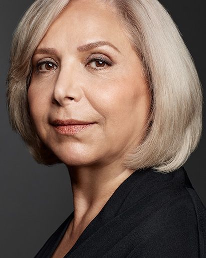 Woman with short blonde hair, brown eyes, and a neutral expression, wearing a black top.