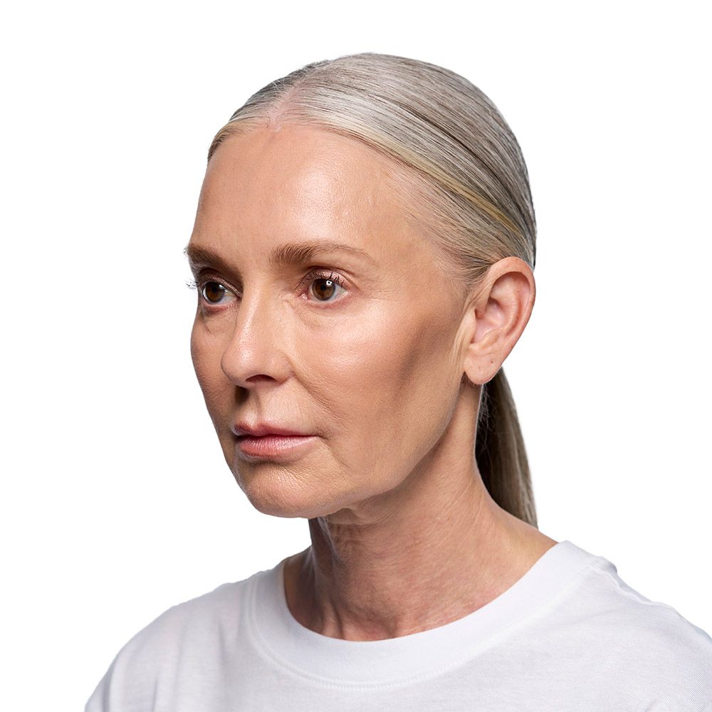 Woman with gray hair in a ponytail, wearing a white shirt, looking to the side.