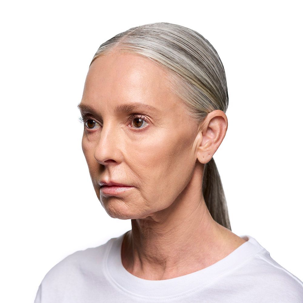 Woman with gray hair in a ponytail, looking to the side, wearing a white t-shirt.