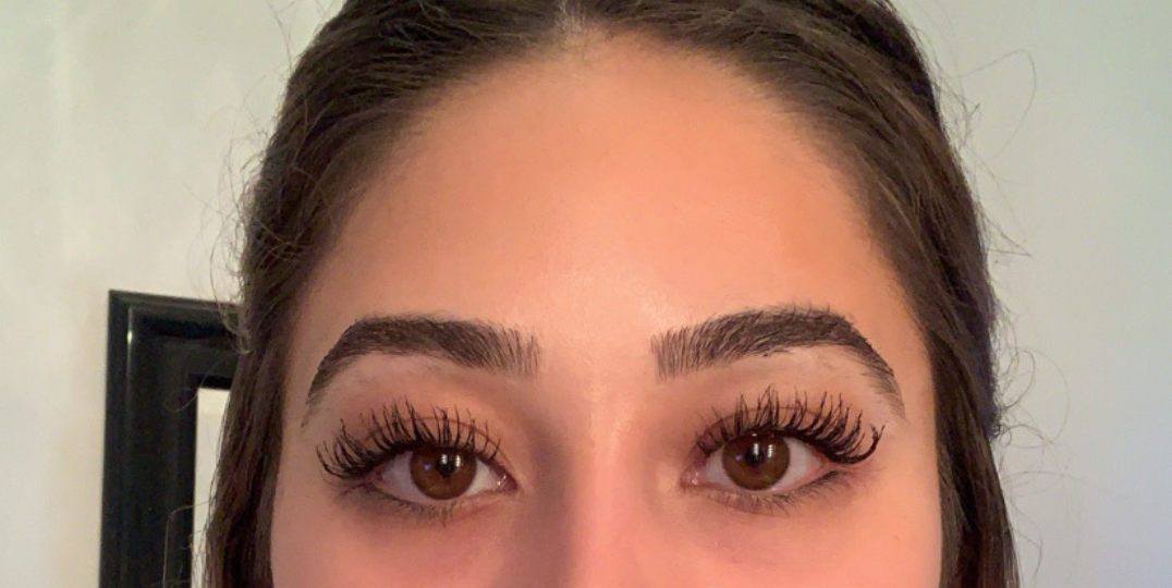 Close-up of a woman's face, showing her eyes with dark eyelashes and neatly shaped eyebrows.