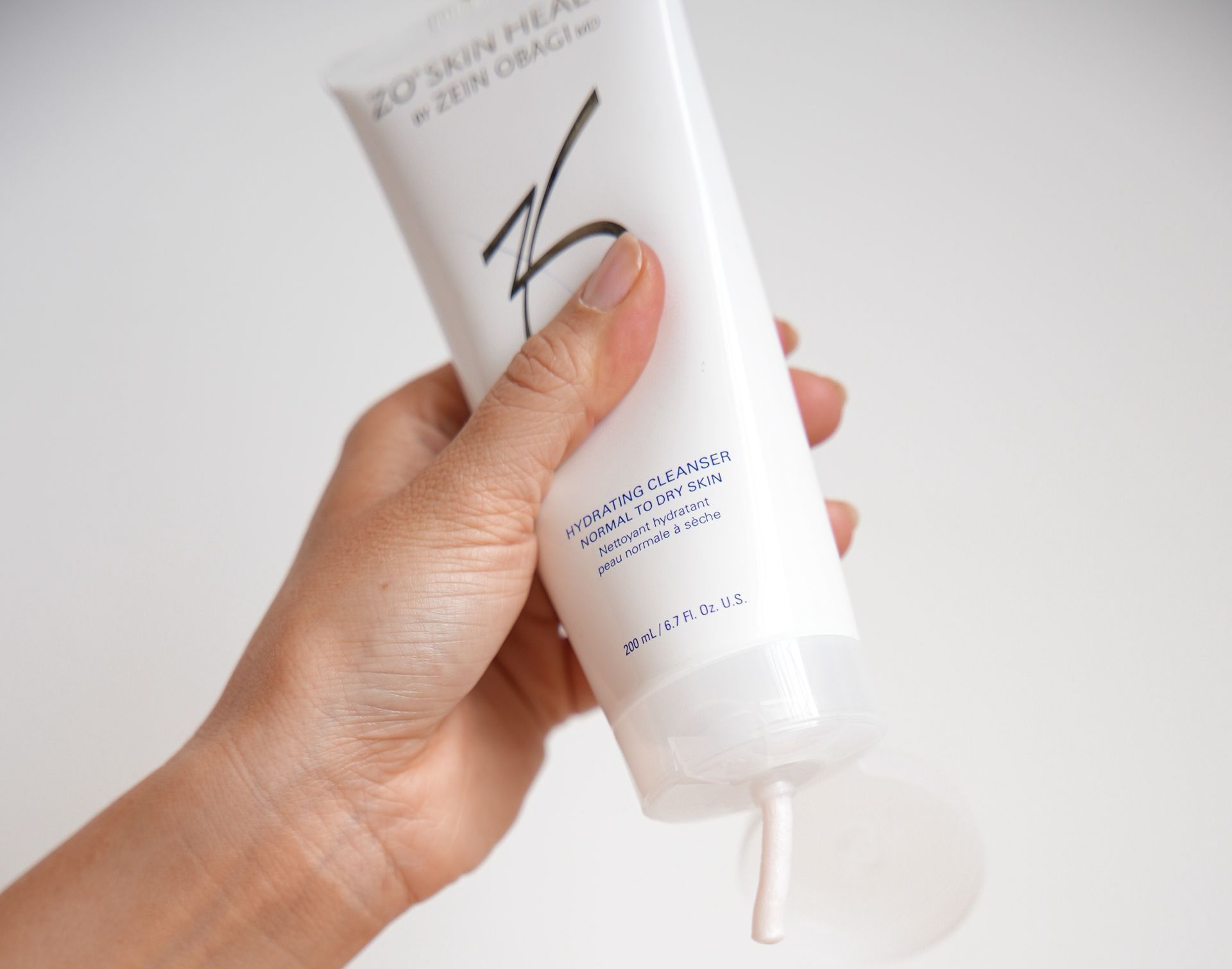Hand squeezing a tube of ZO Skin Health cleanser, dispensing a pink cream.