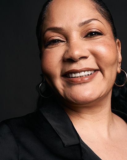 Smiling woman with dark skin, wearing a black jacket and gold hoop earrings.