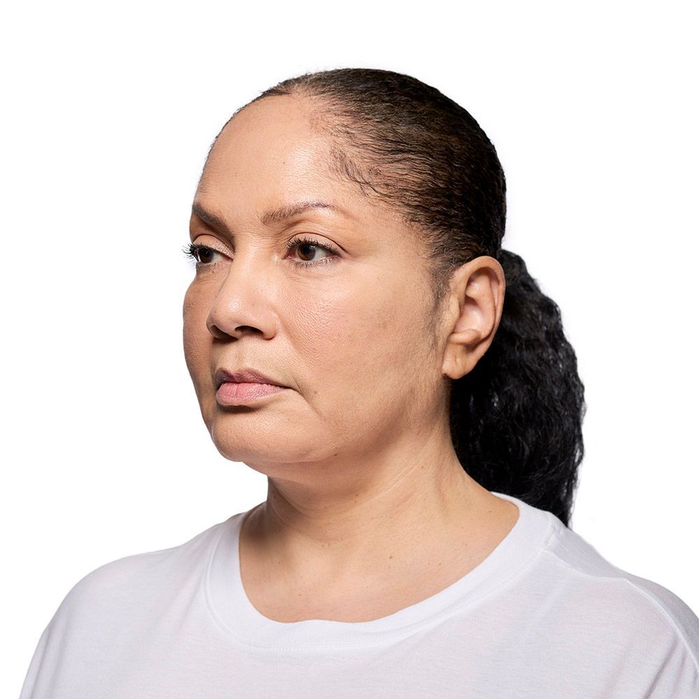 Woman with brown skin and black ponytail looking left, wearing a white shirt.