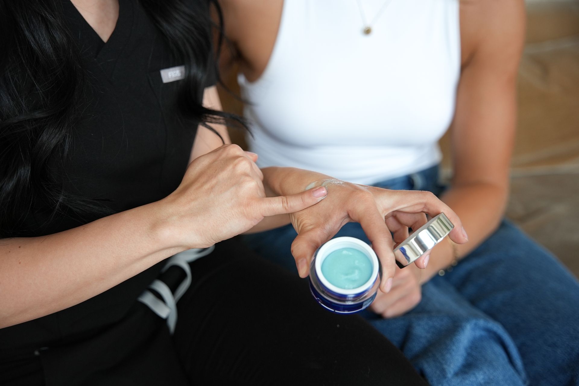 Two people seated close together, one holding a small teal jar and striped tube in their hand