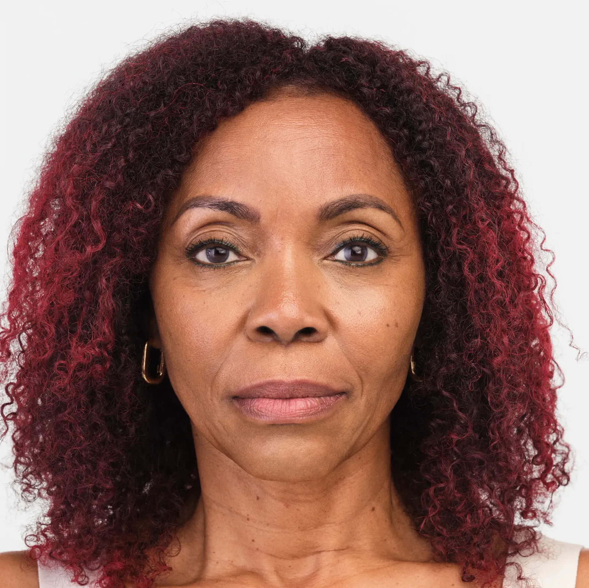 Woman with curly red hair, gold hoop earrings, looking directly at the camera.
