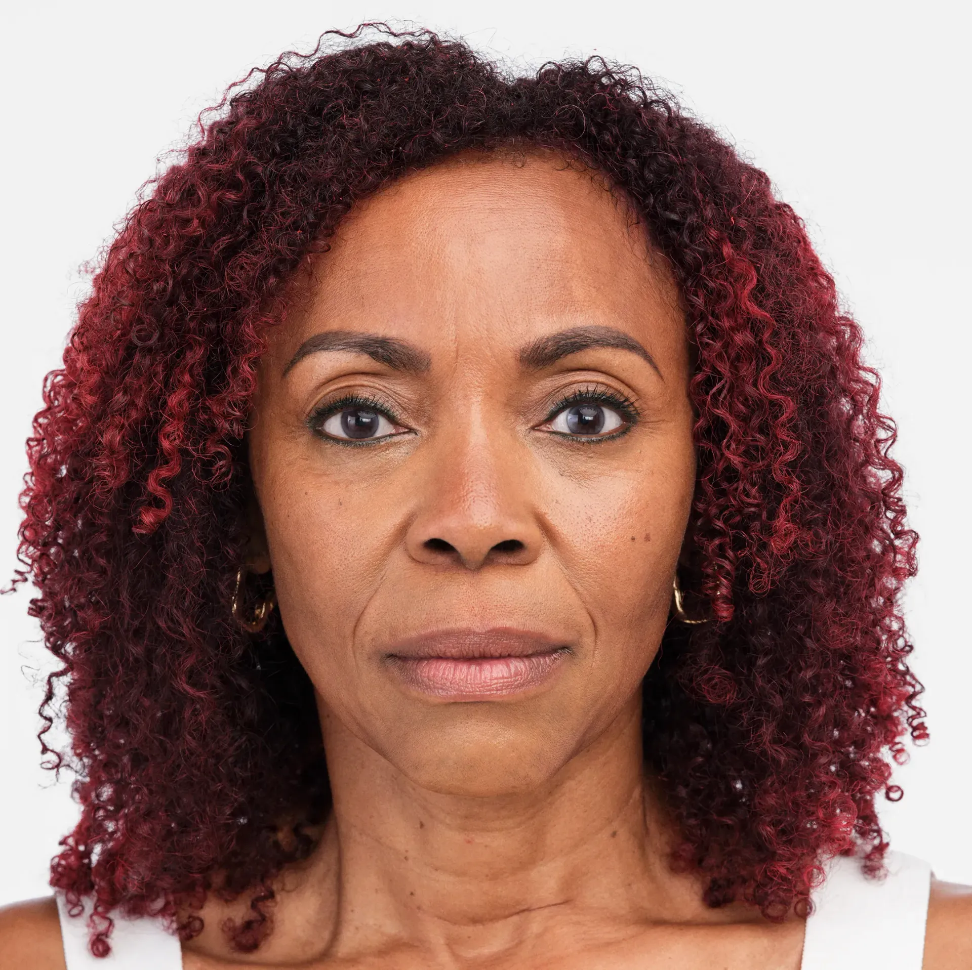 Woman with reddish-brown curly hair and a serious expression.