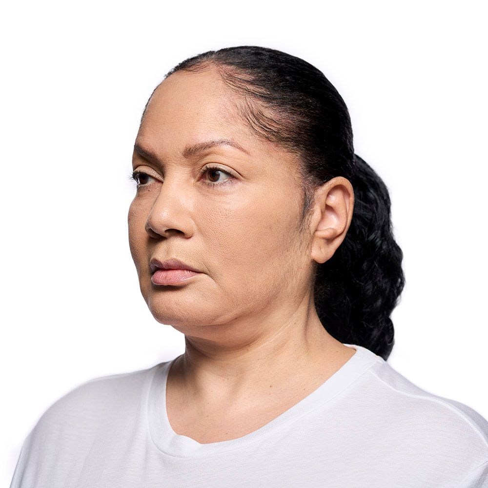 Woman with brown skin and dark hair in a ponytail, looking away, wearing a white t-shirt, against a white background.