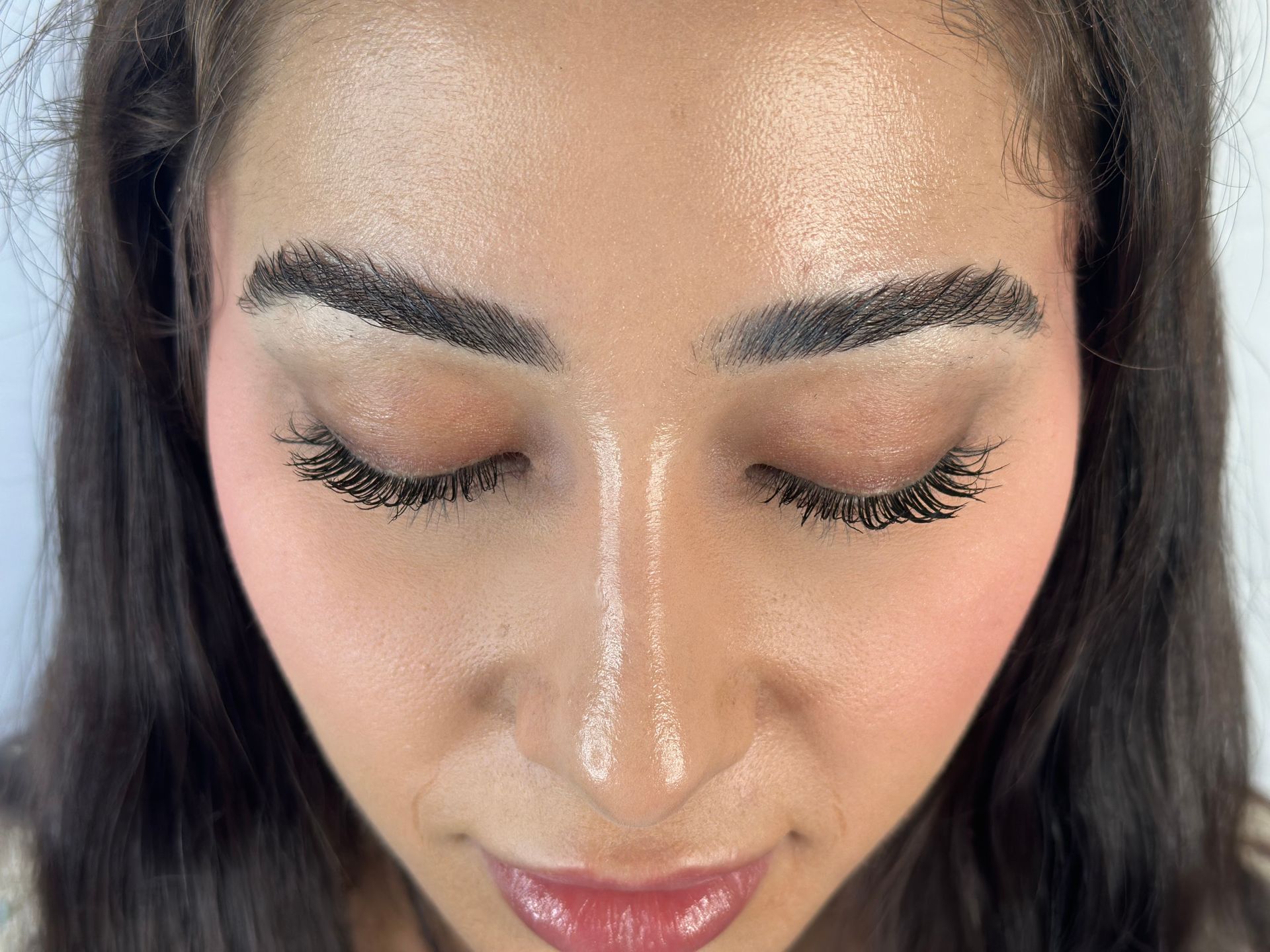 Close-up of a woman with closed eyes, dark eyebrows, long lashes, and pink blush.