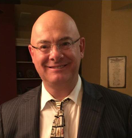 A bald man in a suit and tie smiles for the camera