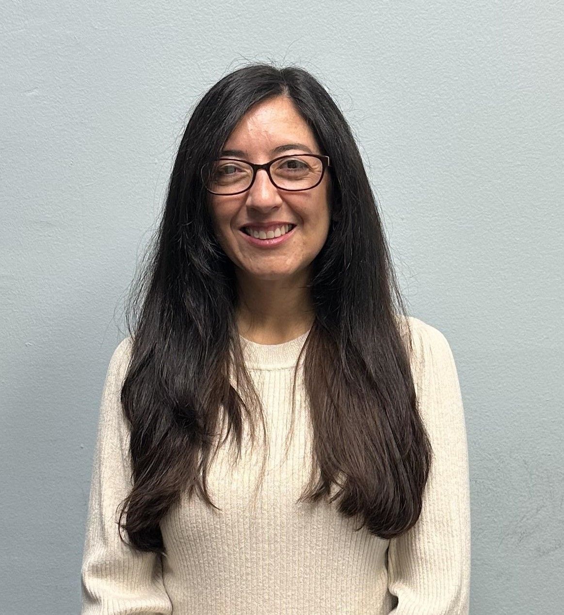 A woman wearing glasses and a white sweater is smiling for the camera.