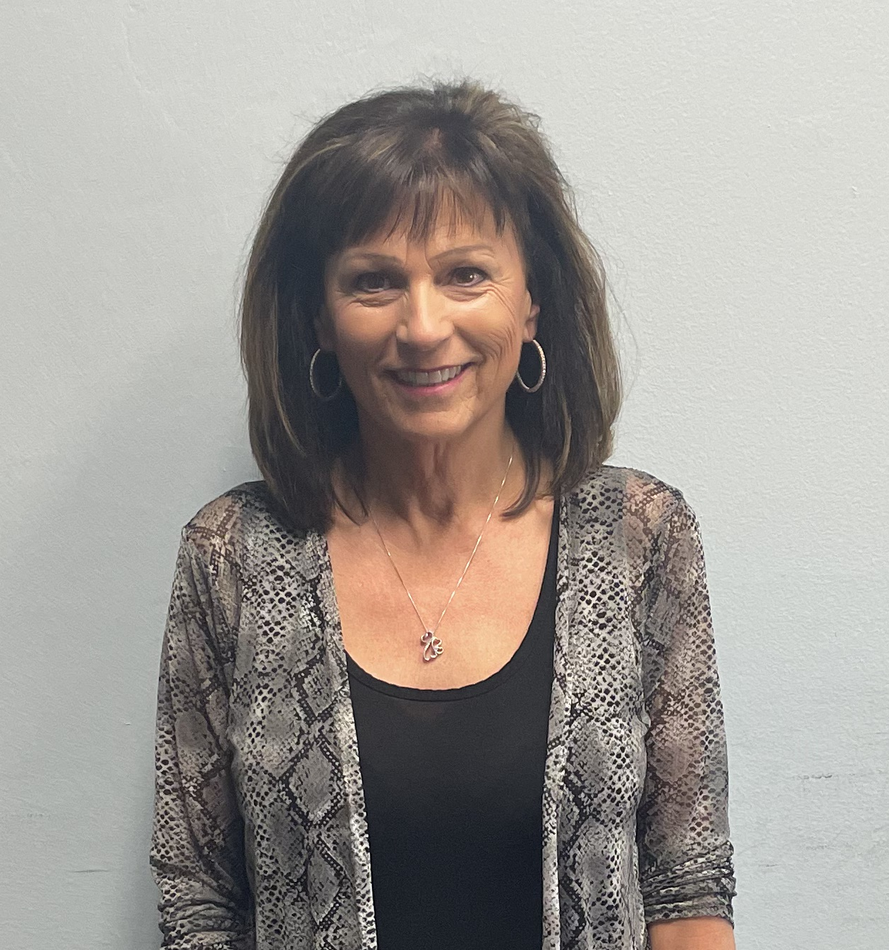 A woman wearing a black shirt and a snake print cardigan is smiling for the camera.