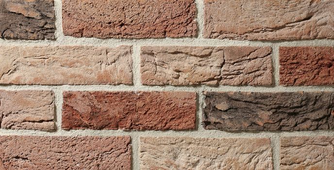 Zbliżenie na ceglaną ścianę z różnymi kolorami cegieł: czerwonymi, brązowymi i jasnobrązowymi, z szarą zaprawą.