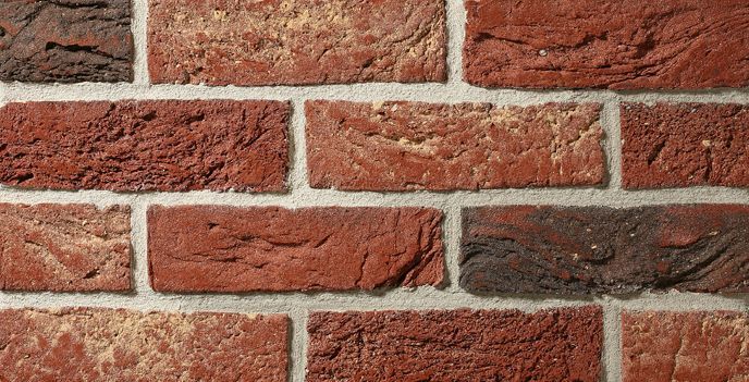 Zbliżenie na ceglaną ścianę z czerwonymi, brązowymi i czarnymi cegłami, widoczne linie zaprawy.