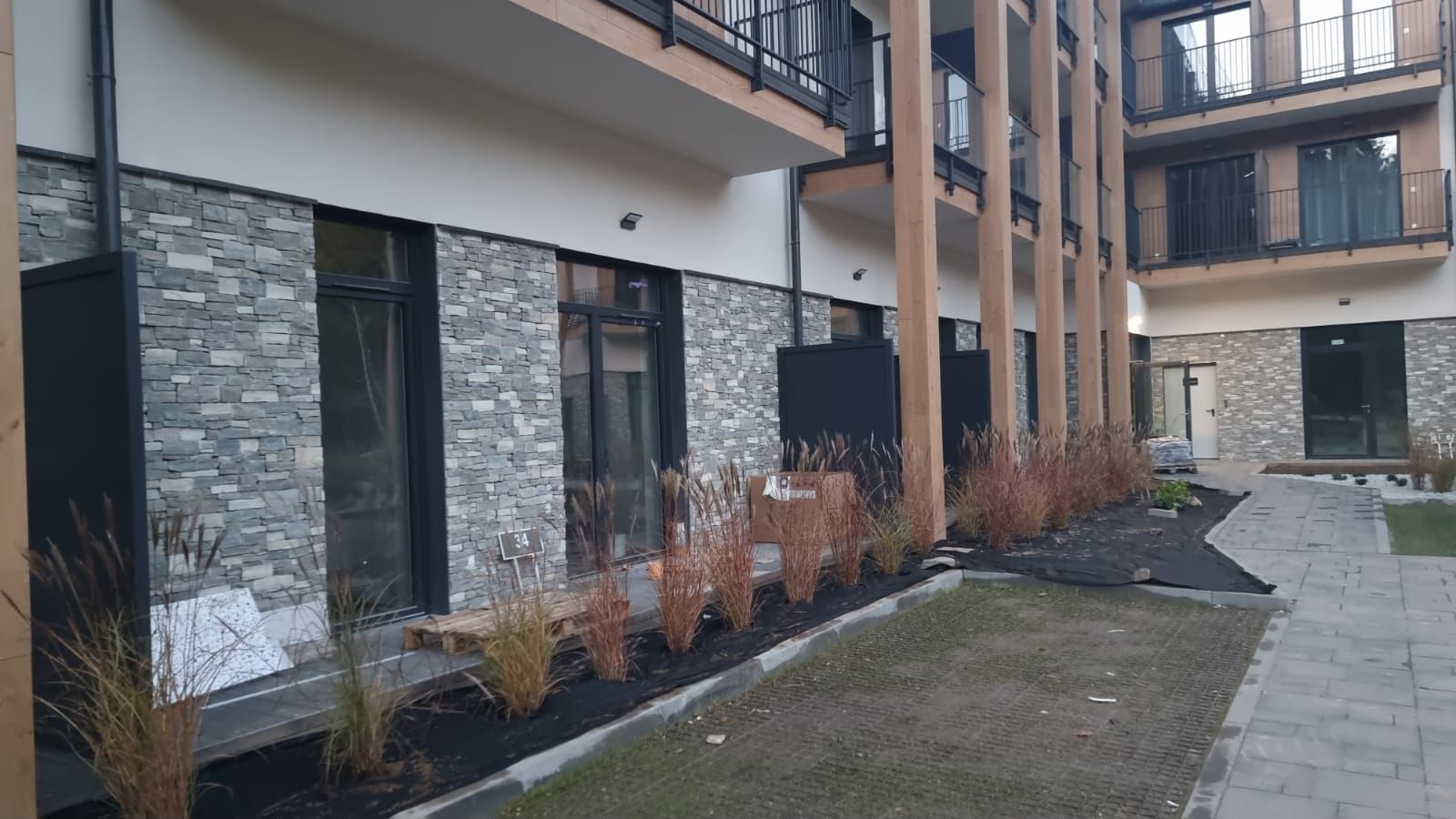 Zewnętrzna część nowoczesnego budynku z kamiennymi akcentami, oknami i zagospodarowaniem terenu.