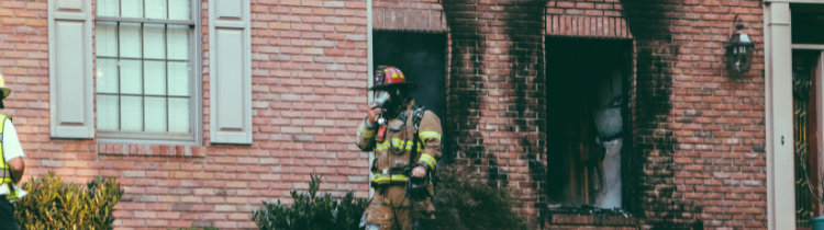 A firefighter is standing in front of a brick house.