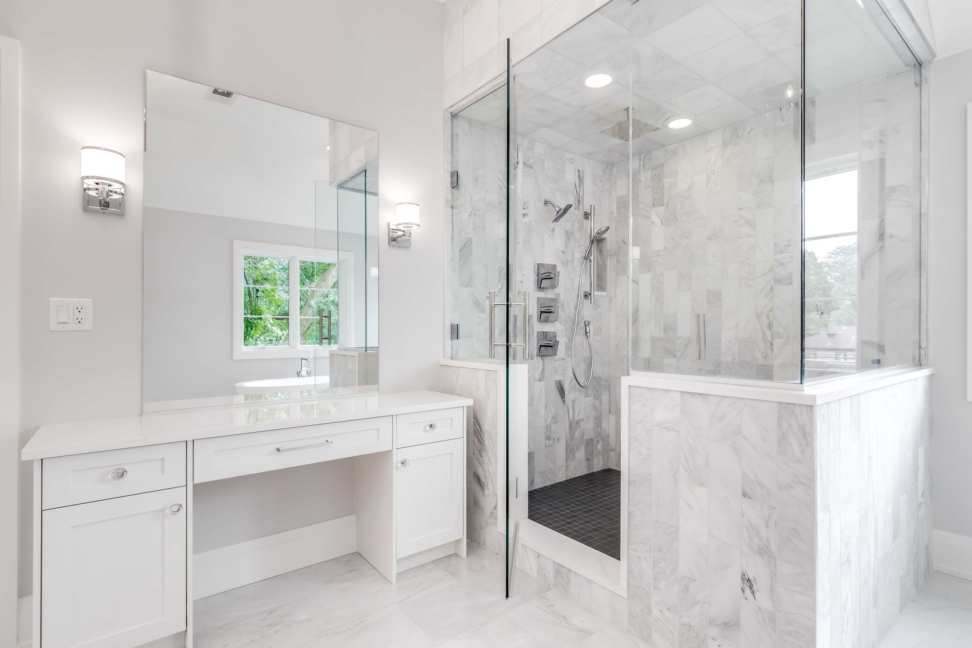 Meuble-lavabo en marbre clair à côté d'une douche vitrée avec carrelage blanc et armoires à miroirs.