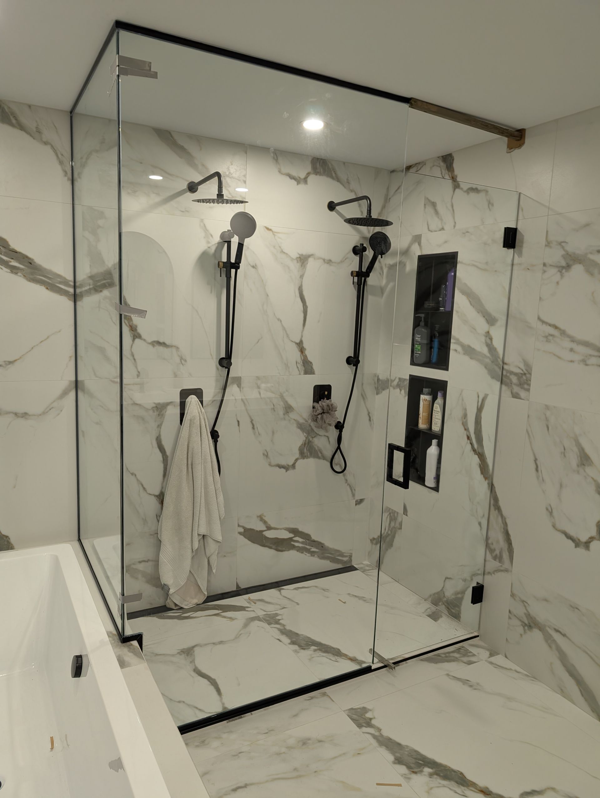 Douche moderne carrelée en marbre avec paroi de verre, double pommeau de douche et niche murale intégrée.