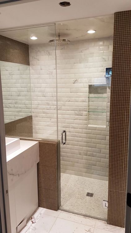 Douche moderne avec carrelage blanc, porte en verre, carreaux décoratifs marron et lavabo sur le côté gauche.