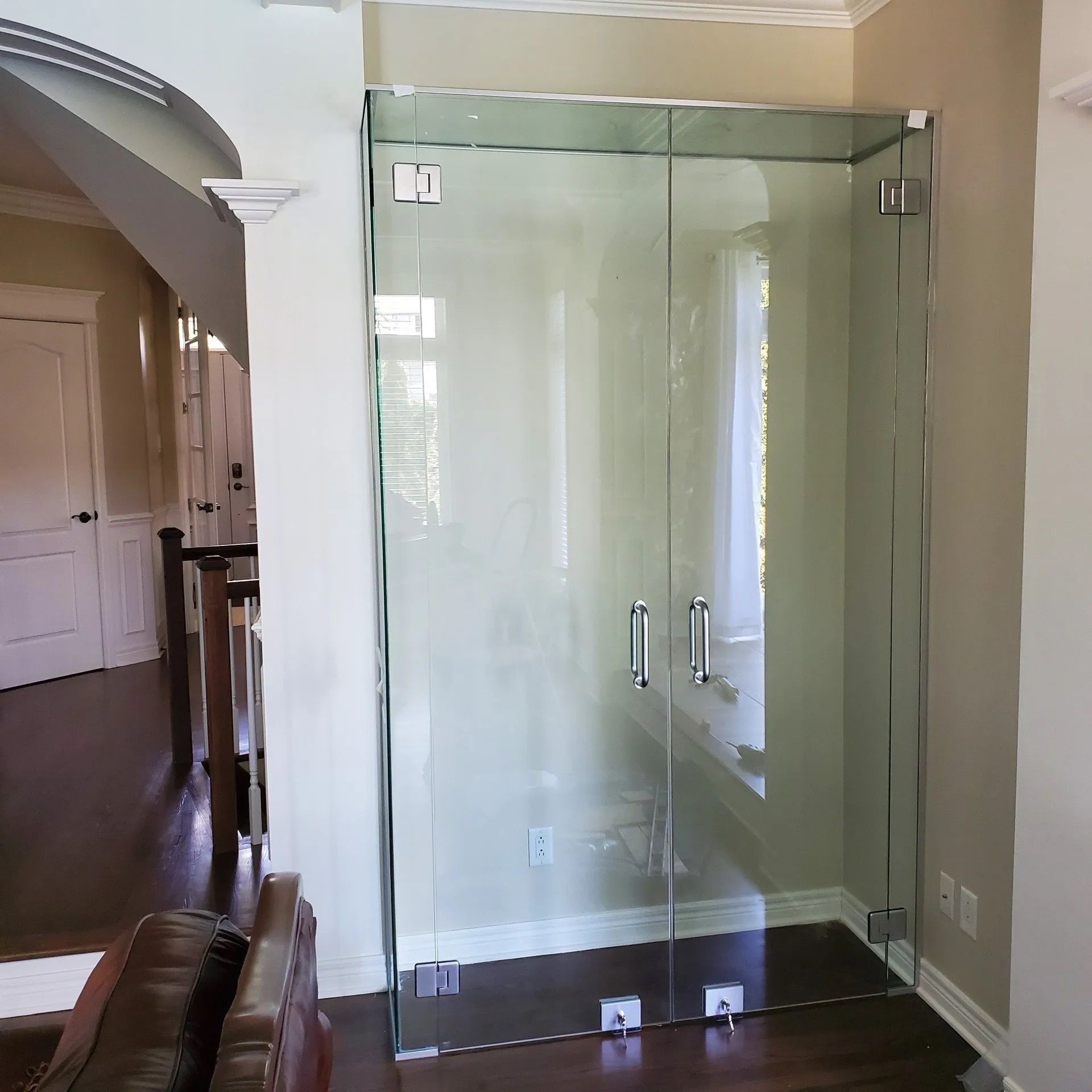 Cabine de douche moderne en verre dans une salle de bains beige avec parquet et porte cintrée