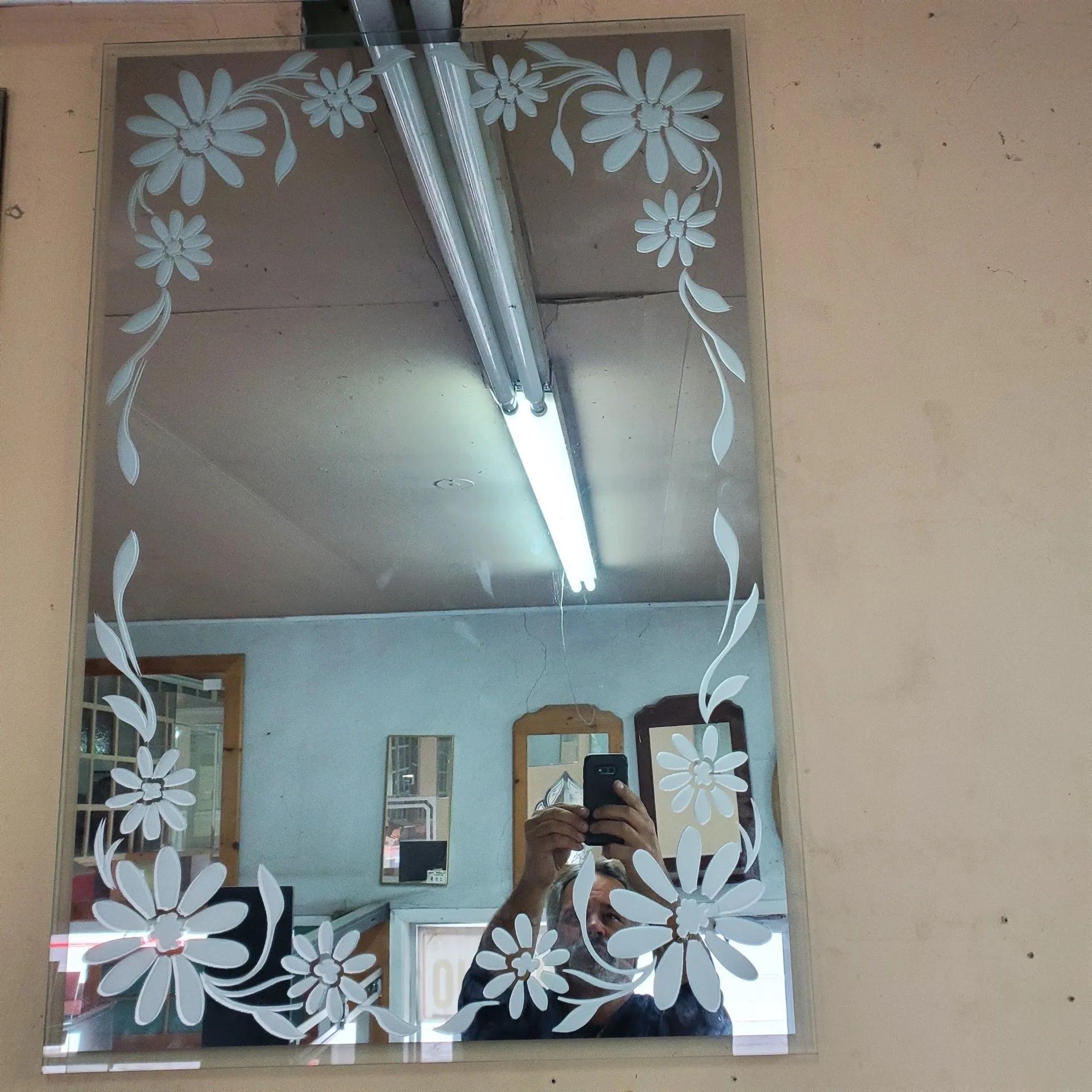 Miroir mural décoratif à bordure florale blanche reflétant une pièce et des néons au plafond