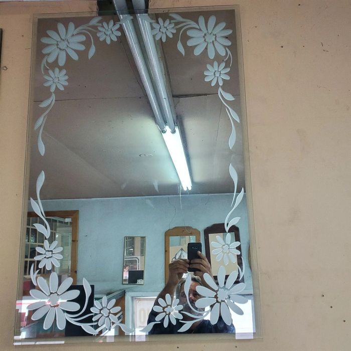 Miroir mural décoratif à bordure florale blanche reflétant une pièce et des néons au plafond