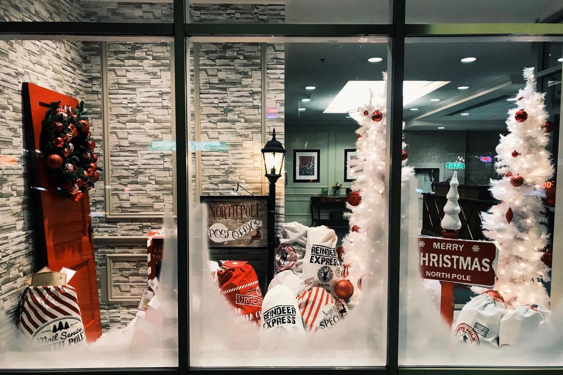 Vitrine de Noël avec sapins blancs, touches de rouge et coussins festifs.