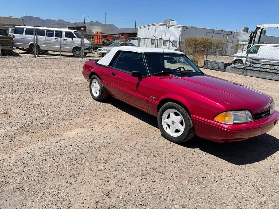 A red mustang convertible is parked in a dirt lot.