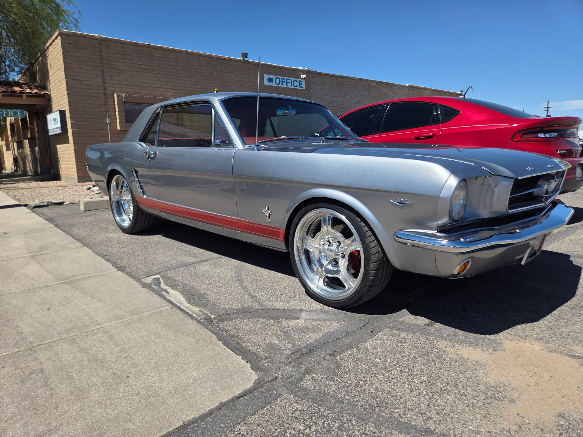 Silver classic muscle car parked outside a building with a red car behind it