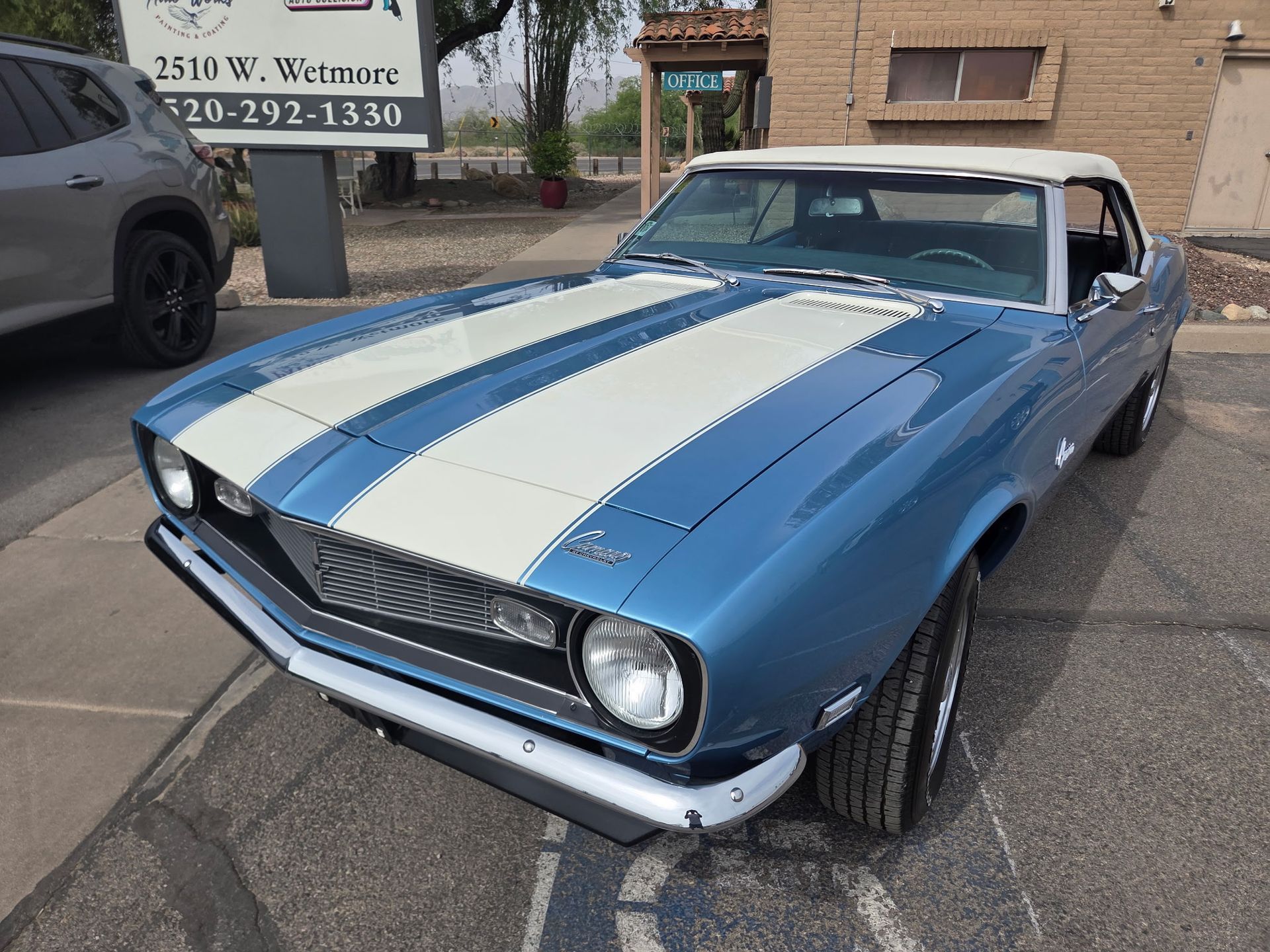 Blue classic convertible with white racing stripes parked outdoors on a street.