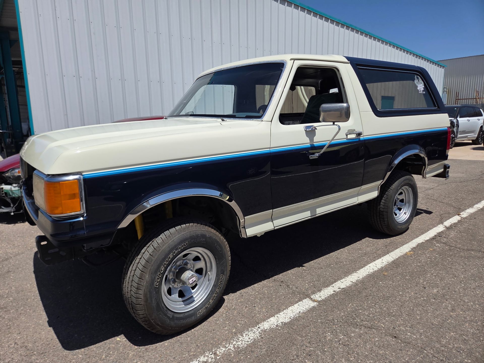Two-tone blue and white classic SUV parked beside a metal building in sunlight