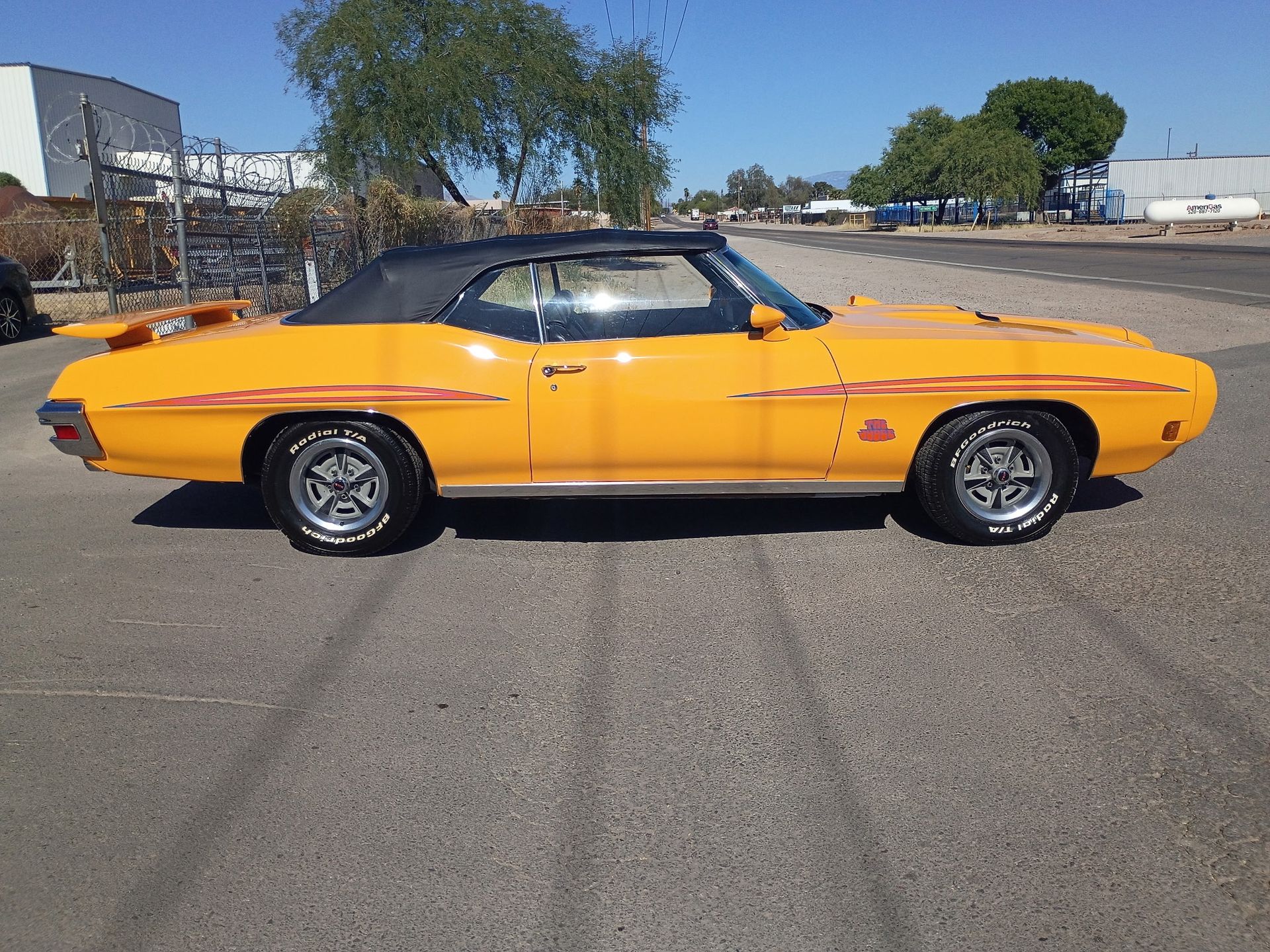 Orange classic car parked on a paved lot under a blue sky