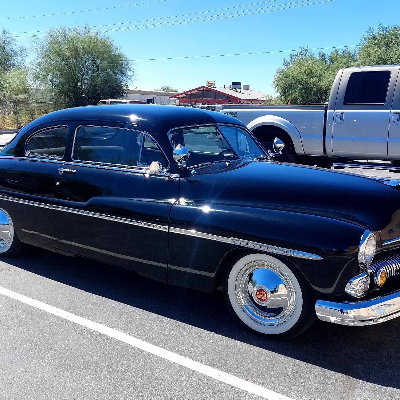 A black car is parked in a parking lot next to a silver truck
