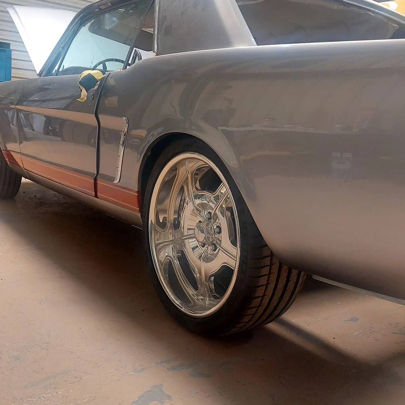 A gray car with chrome wheels is parked in a garage