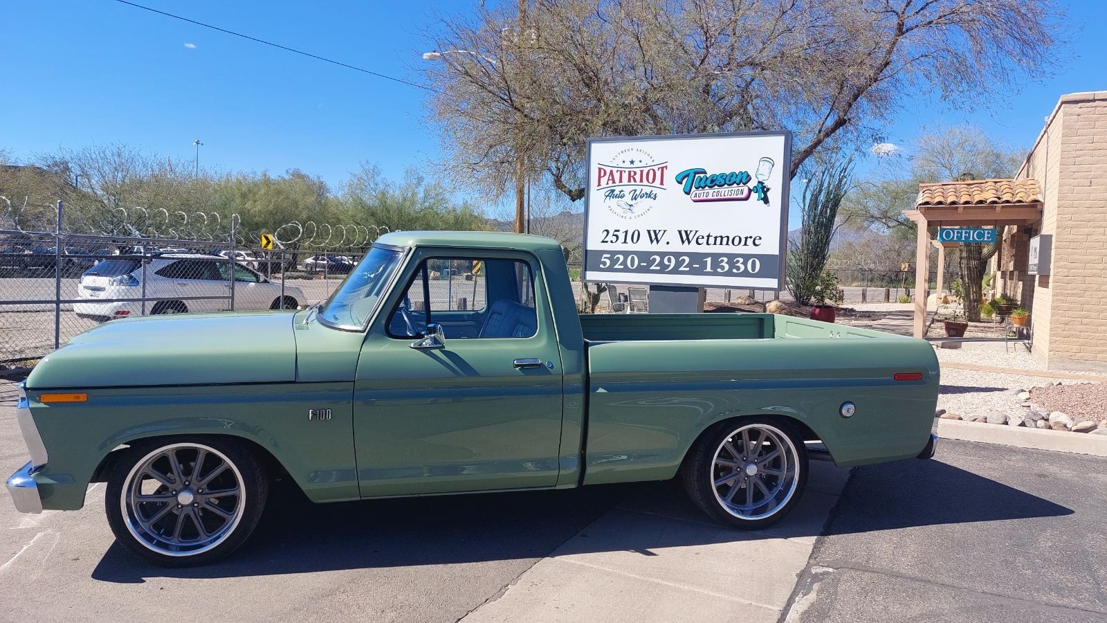 A green truck is parked in front of a building next to a sign.