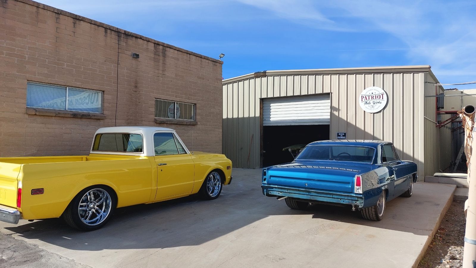 A yellow truck and a blue car are parked in front of a building.