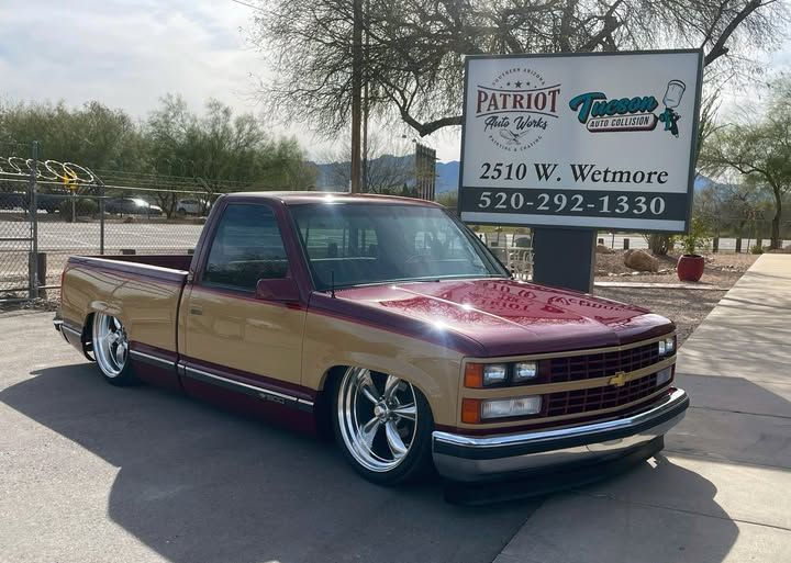 a classic chevy car in front of the patriot auto works sign