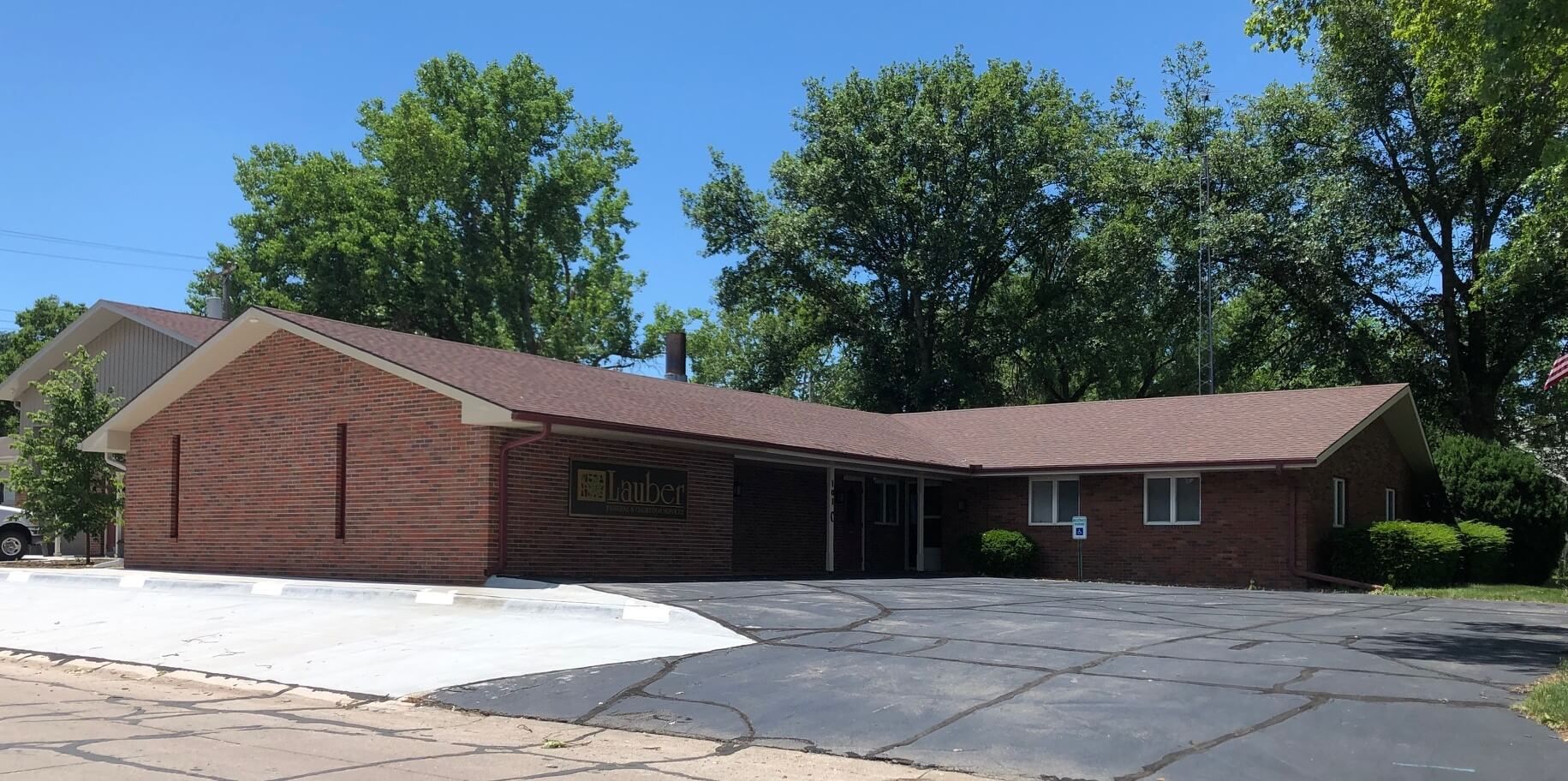 Single-story brick building with a wide driveway and large trees on a sunny day